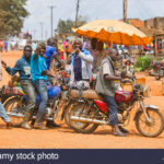 small-town-street-scene-men-with-motorcycles-local-transport-motorbike-taxis-uganda-east-africa-PJKTD1